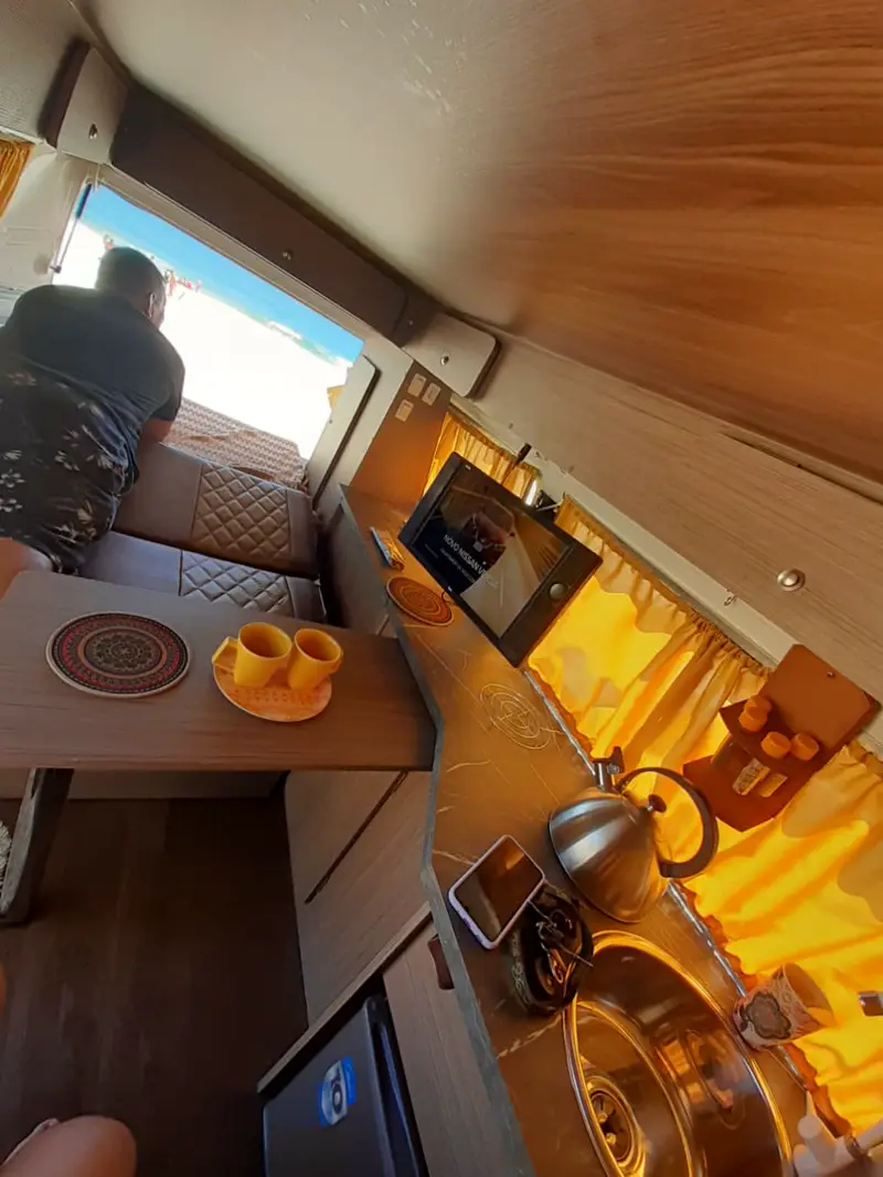 Interior de Kombi montada pela Camper RJ, com mesa, cozinha e cortinas amarelas