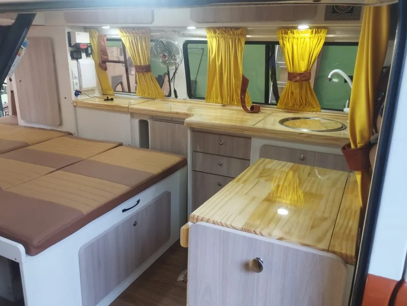 Interior de Kombi montada pela Camper RJ, com cama, bancada em madeira e cortinas amarelas
