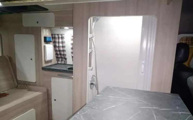 Interior de Kombi montada pela Camper RJ, com banheiro, bancada de pedra escura e cama de casal
